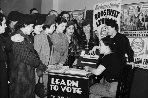 Women surrounded by posters in English and Yiddish supporting Franklin D. Roosevelt, Herbert H. Lehman, and the American Labor Party teach other women how to vote, 1935. International Ladies Garment Workers Union Photographs (1885-1985)